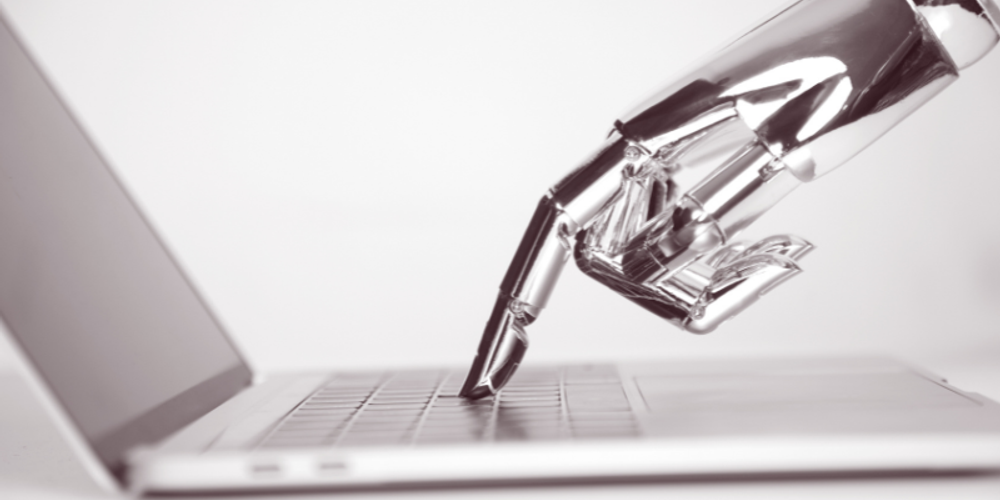 A robotic hand is typing on a laptop computer.