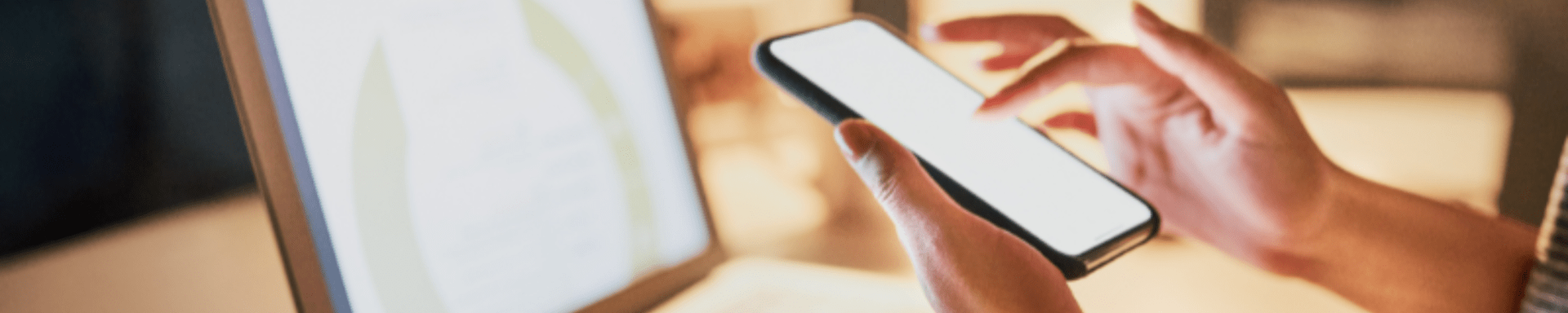 A person is holding a cell phone in front of a computer screen.