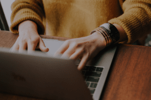 A person is typing on a laptop computer on a wooden table.