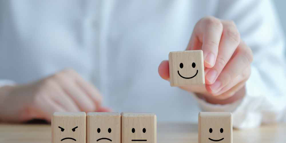 A person is holding a wooden block with a smiley face on it.