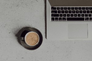 A cup of coffee is sitting next to a laptop computer on a table.