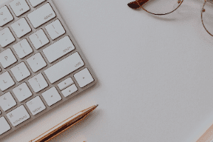 A keyboard , pencil and glasses are on a white table.