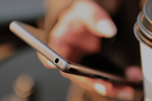 A person is using a cell phone next to a cup of coffee