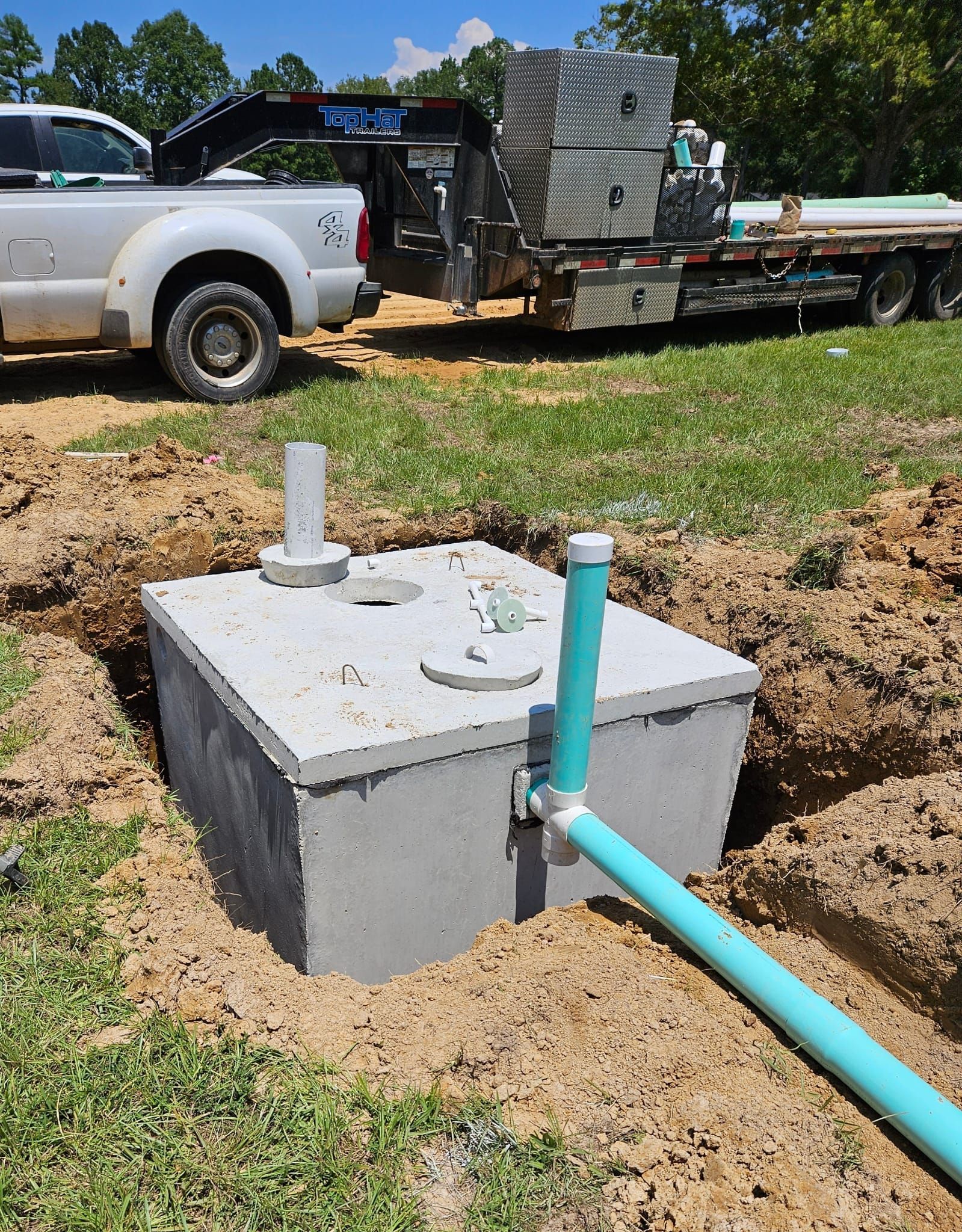 Two green circular septic tank risers installed in a grassy, excavated area with piles of dirt and a vertical pipe nearby.