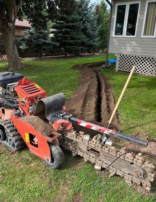 A corrugated metal culvert with vertical metal bars embedded in a stone and mortar headwall set into a grassy hillside.