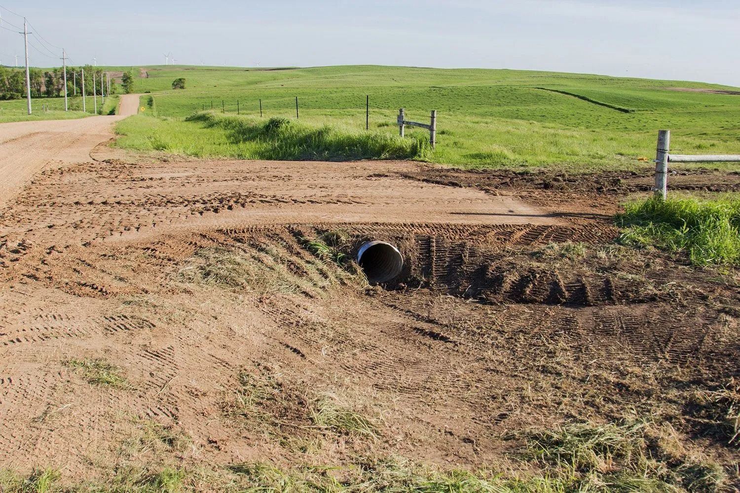 A concrete septic tank installed in a trench in a grassy field, with a laser level on a tripod nearby.