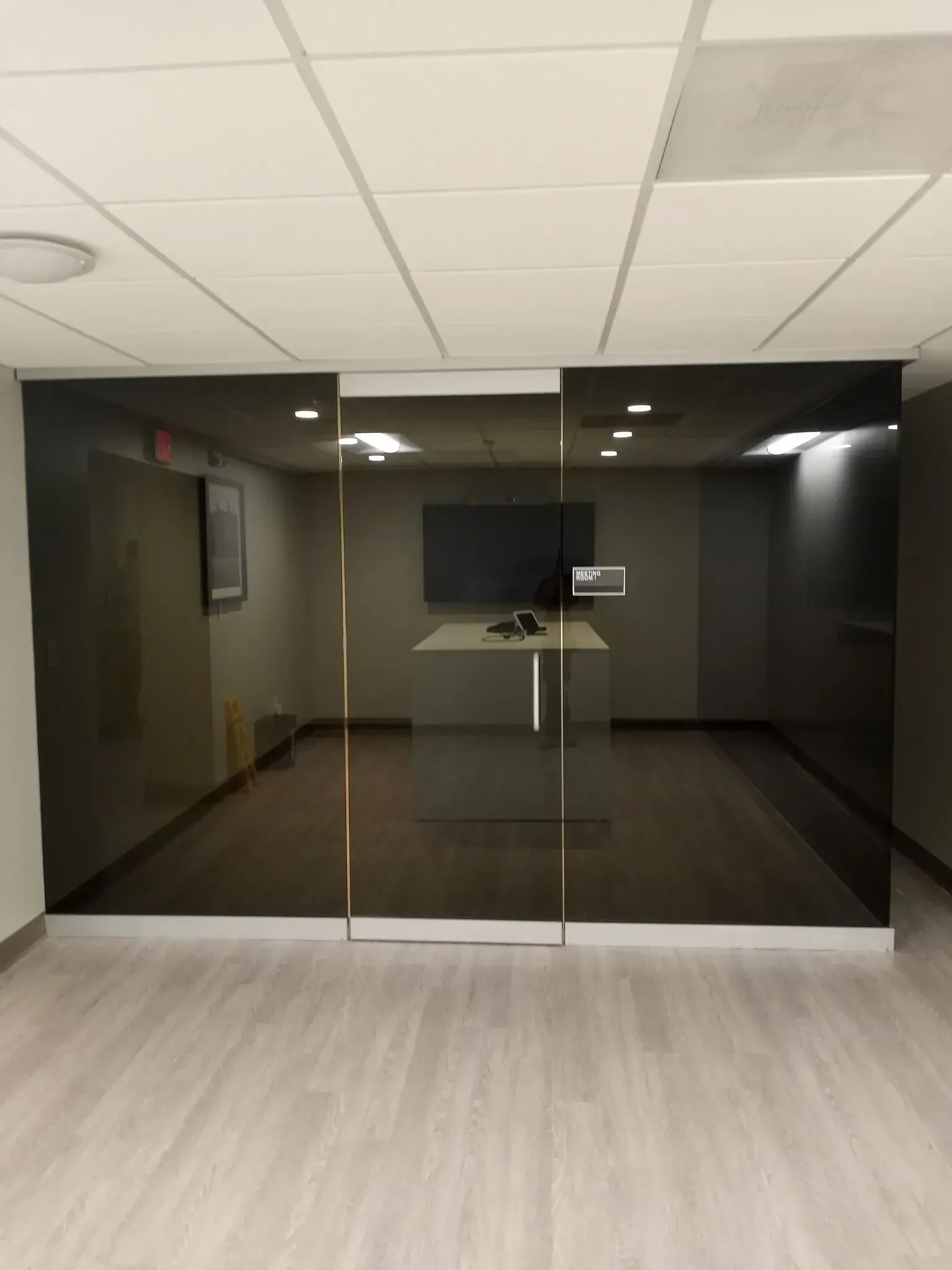 Empty office lobby with glass double doors, dark walls, and a wall-mounted TV.
