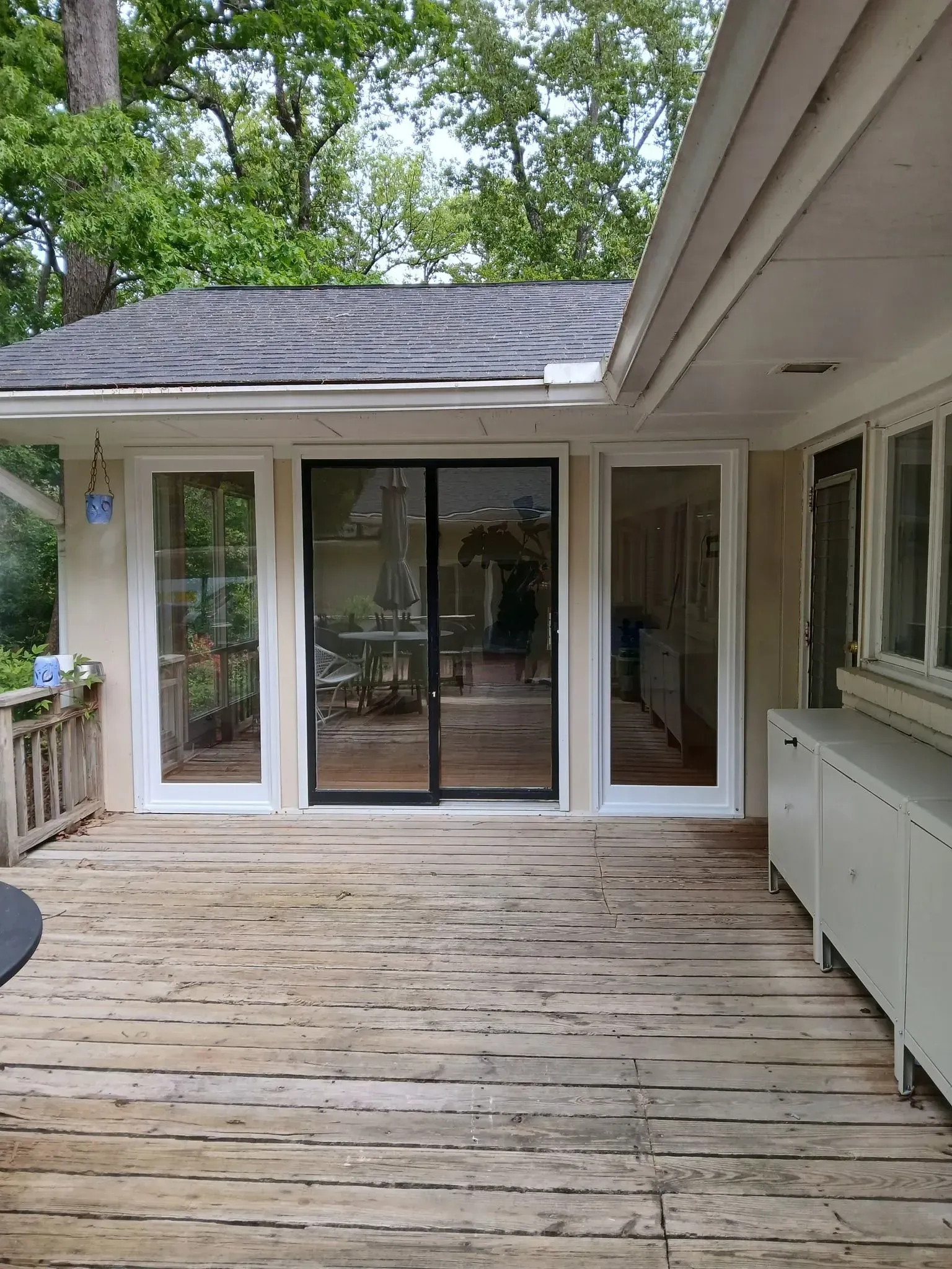 Weathered wooden deck outside a house, with sliding glass doors and screened windows under a covered roof