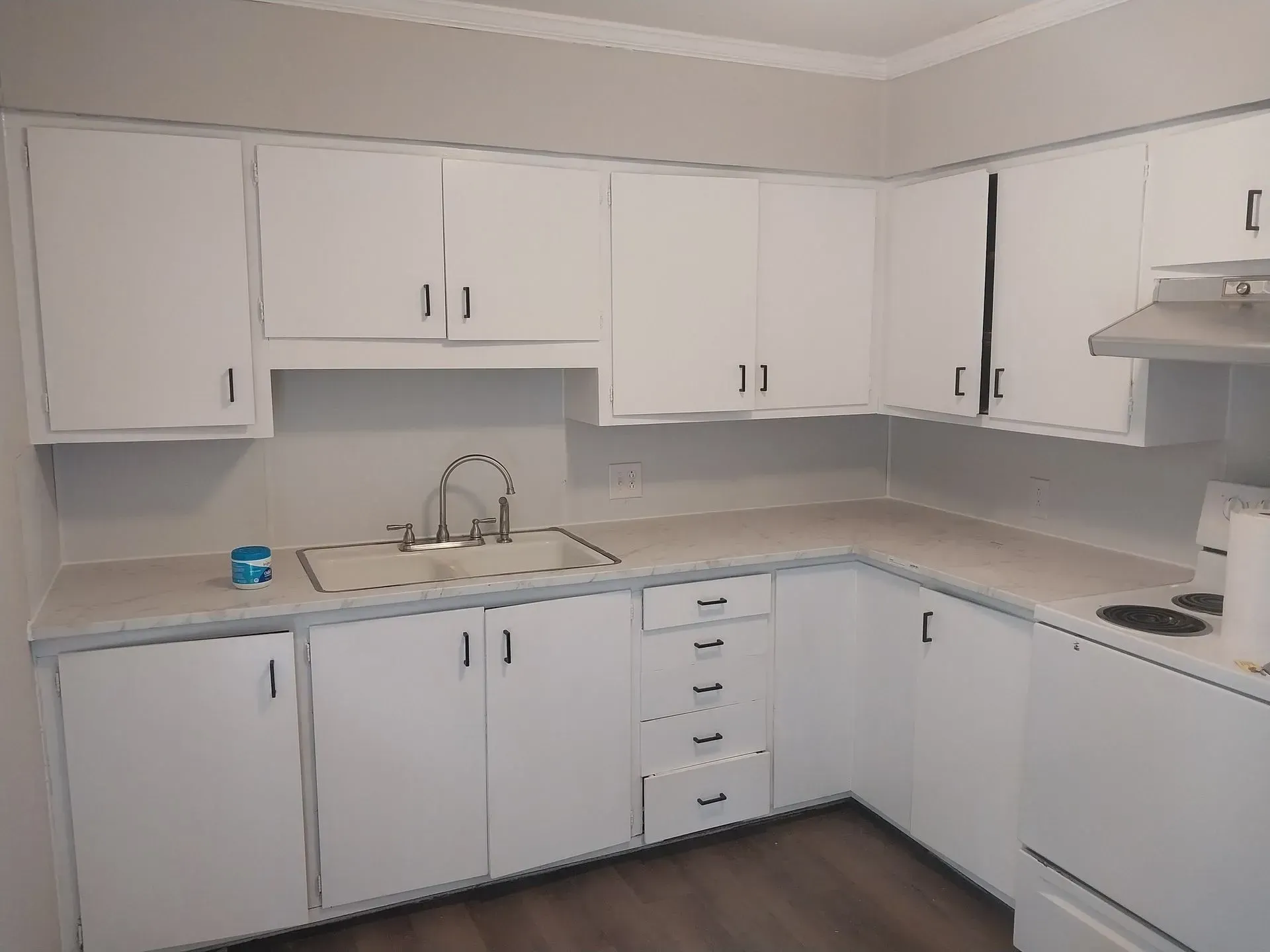 White L-shaped kitchen with cabinets, gray countertops, sink, and stove in a clean, empty room