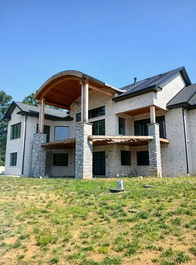 Large modern house under construction with stone exterior, arched porch, and grassy front yard