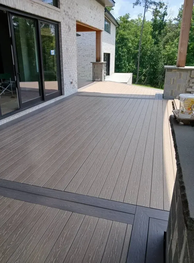 Modern patio with gray composite decking beside a house and sliding glass doors, bordered by stone walls.