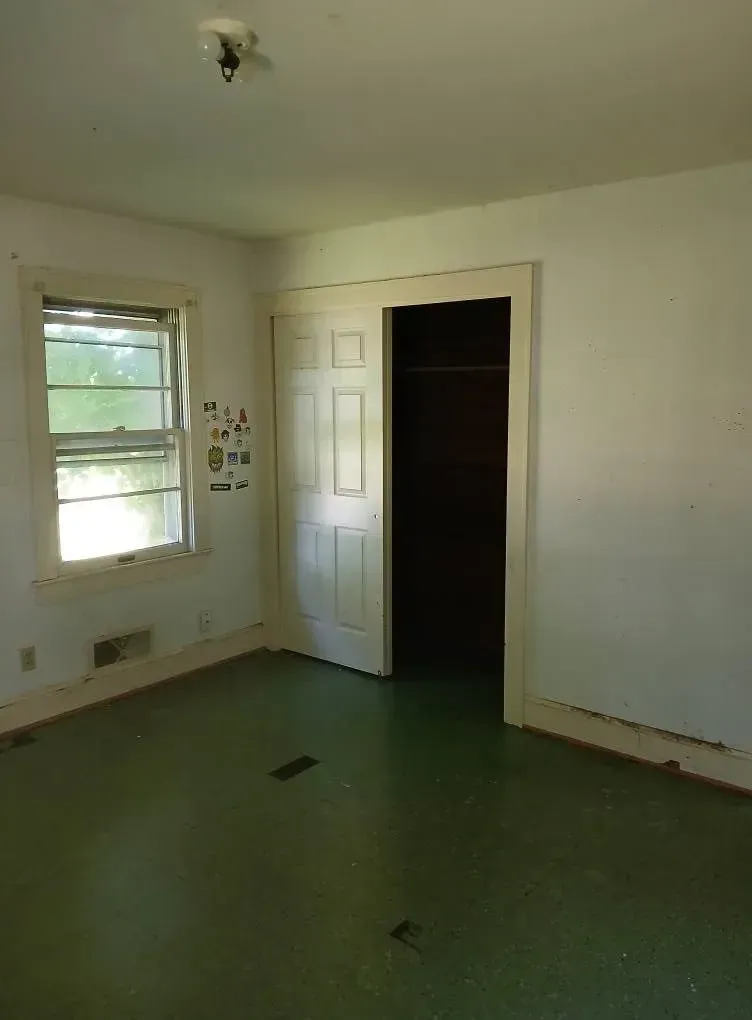 Empty room with white walls, green floor, one window, and an open closet door