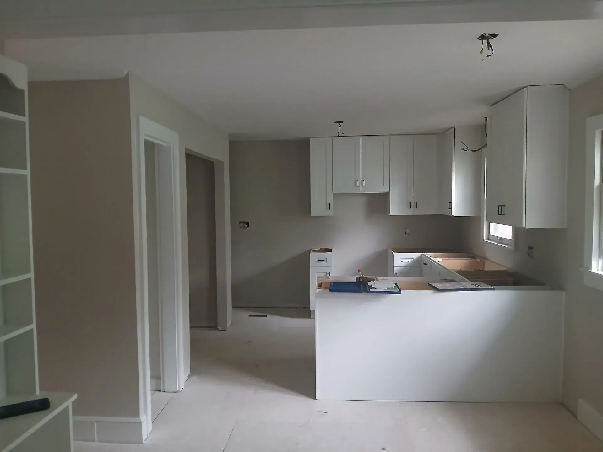 Empty kitchen and living area with white cabinets, gray countertops, and unfinished floors.