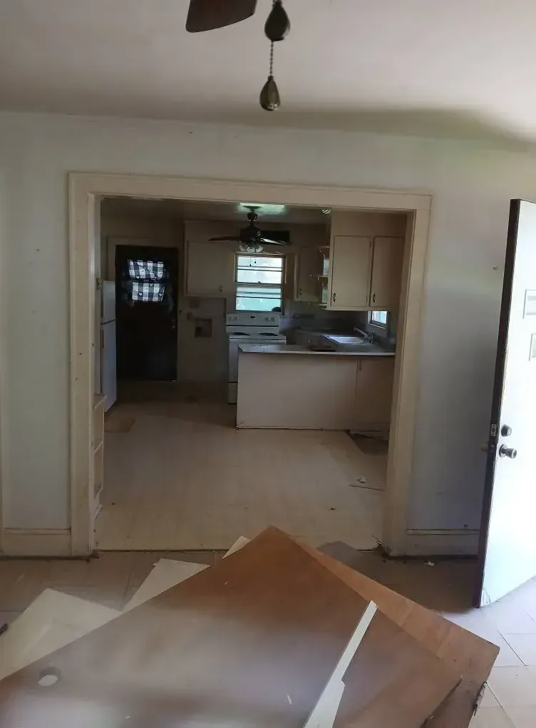 Empty room with a doorway opening to a small kitchen, and cardboard debris on the floor in the foreground