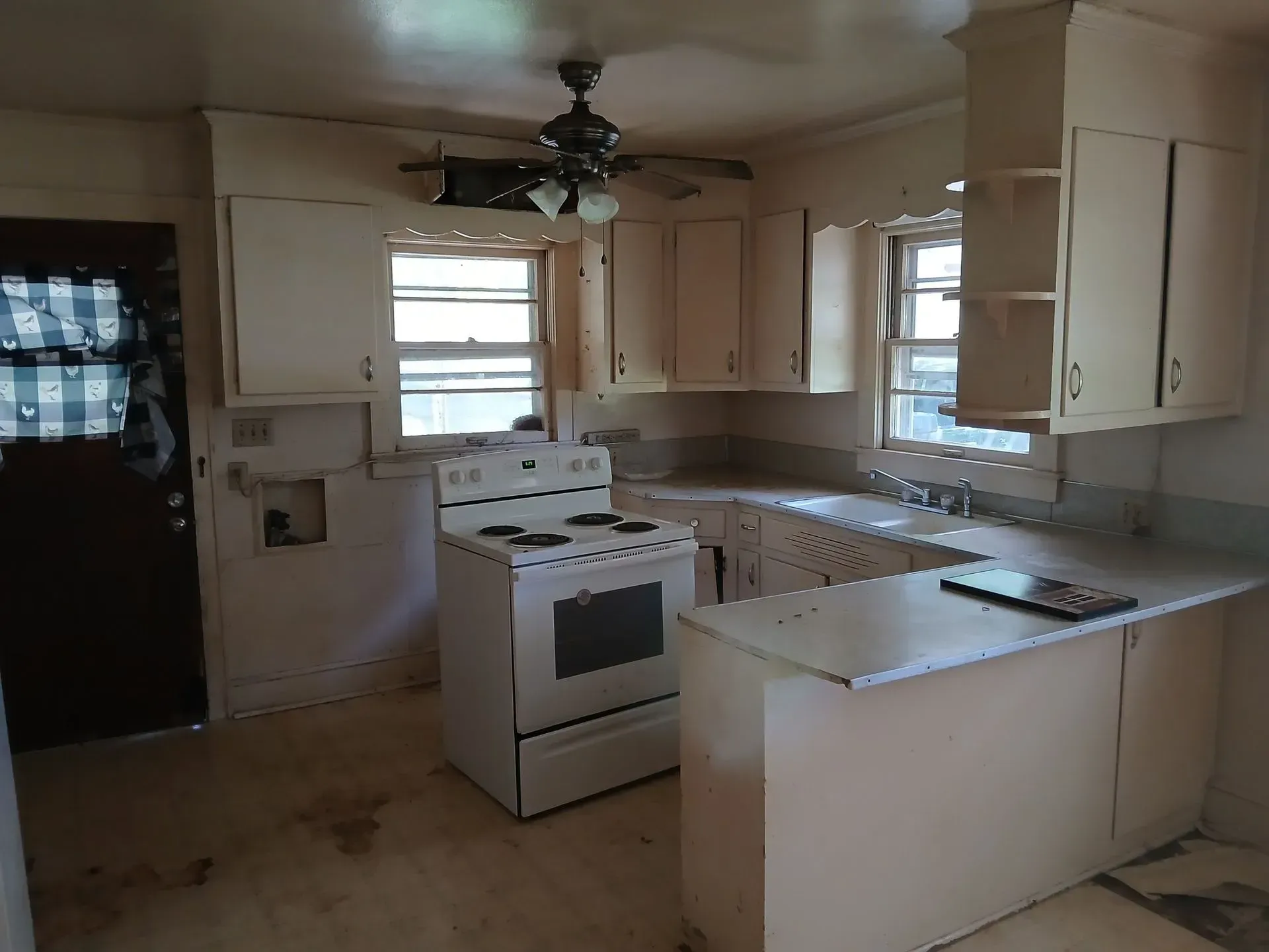 Small kitchen with white cabinets, stove, island counter, and windows; a ceiling fan hangs overhead.