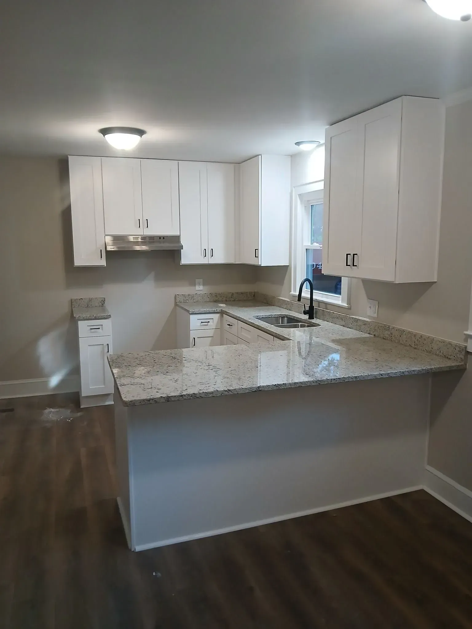 Empty kitchen with white cabinets, granite countertops, and a breakfast bar.
