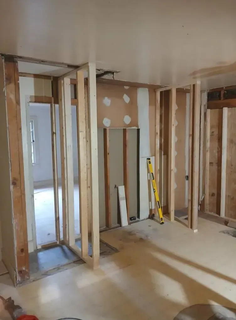 Partially framed room under renovation with exposed studs, drywall patches, and tools leaning against the wall