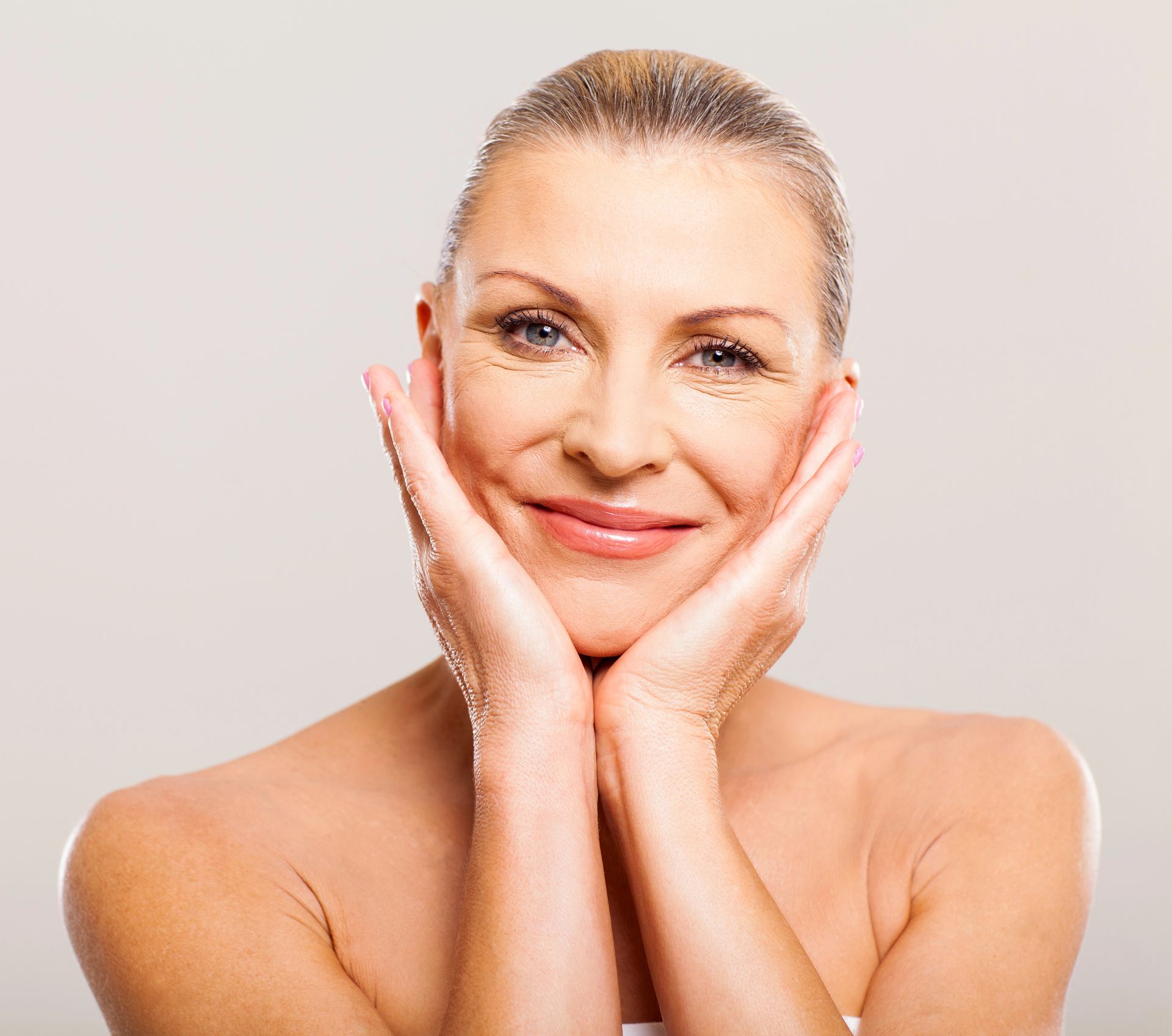 A woman is smiling with her hands on her face.