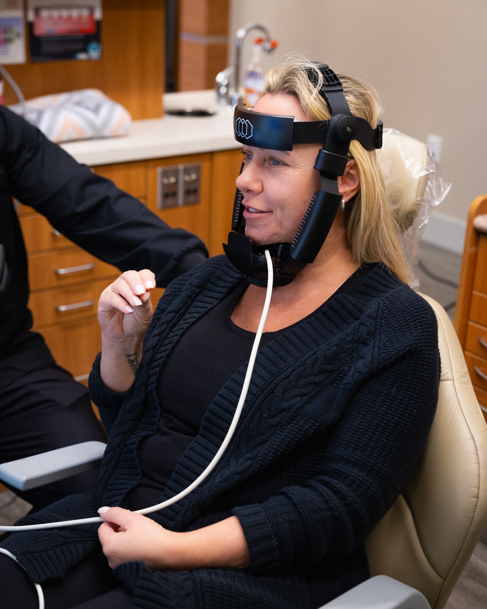 A woman wearing a device on her head is sitting in a dental chair receiving a Define treatment.