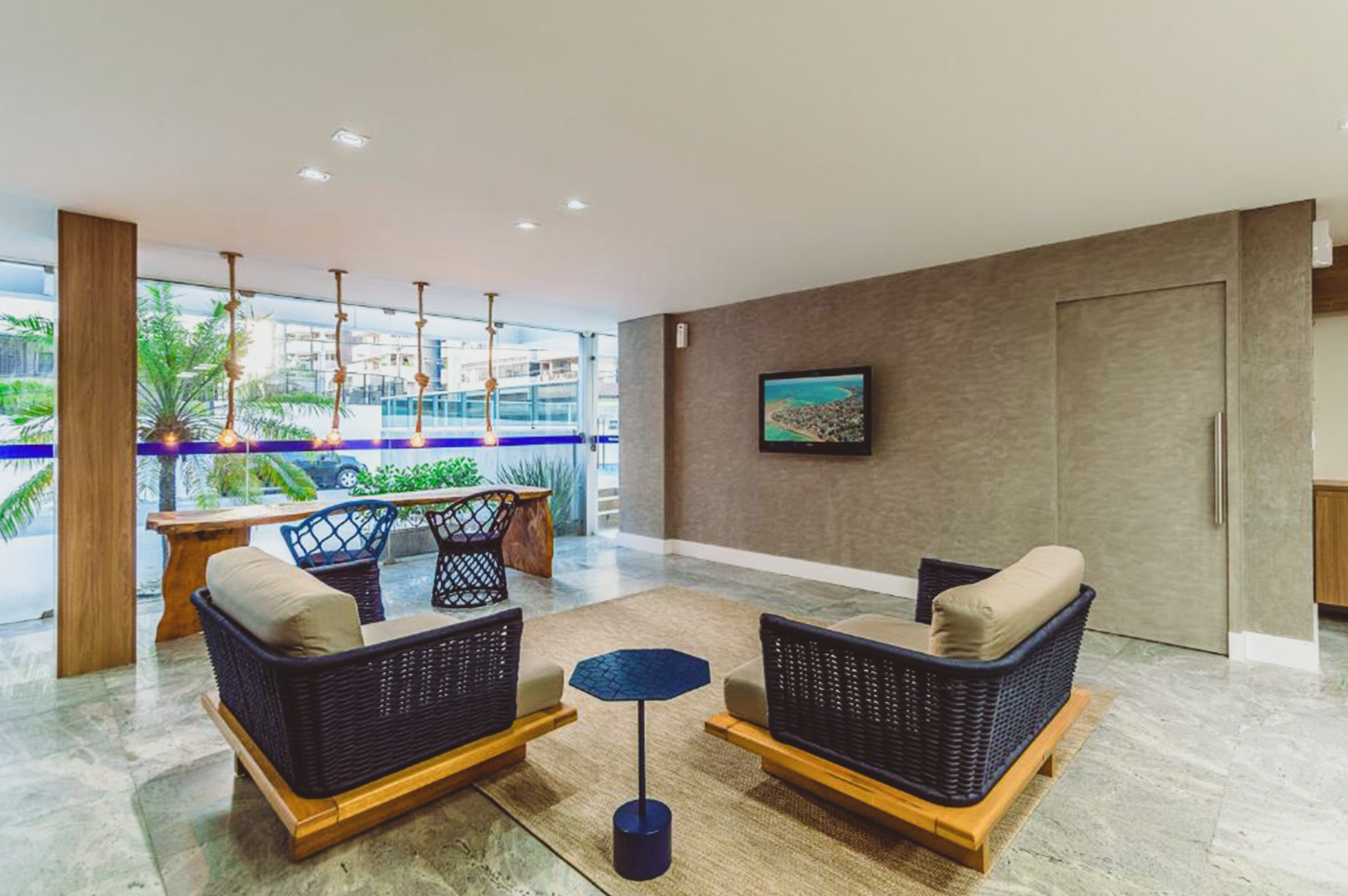 Sala de estar com duas poltronas, uma mesa pequena, tapete e uma TV montada em uma parede texturizada.