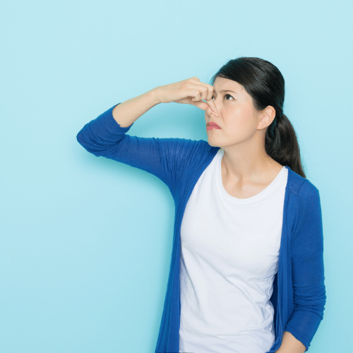 A woman covering her nose with her hand against a blue wall