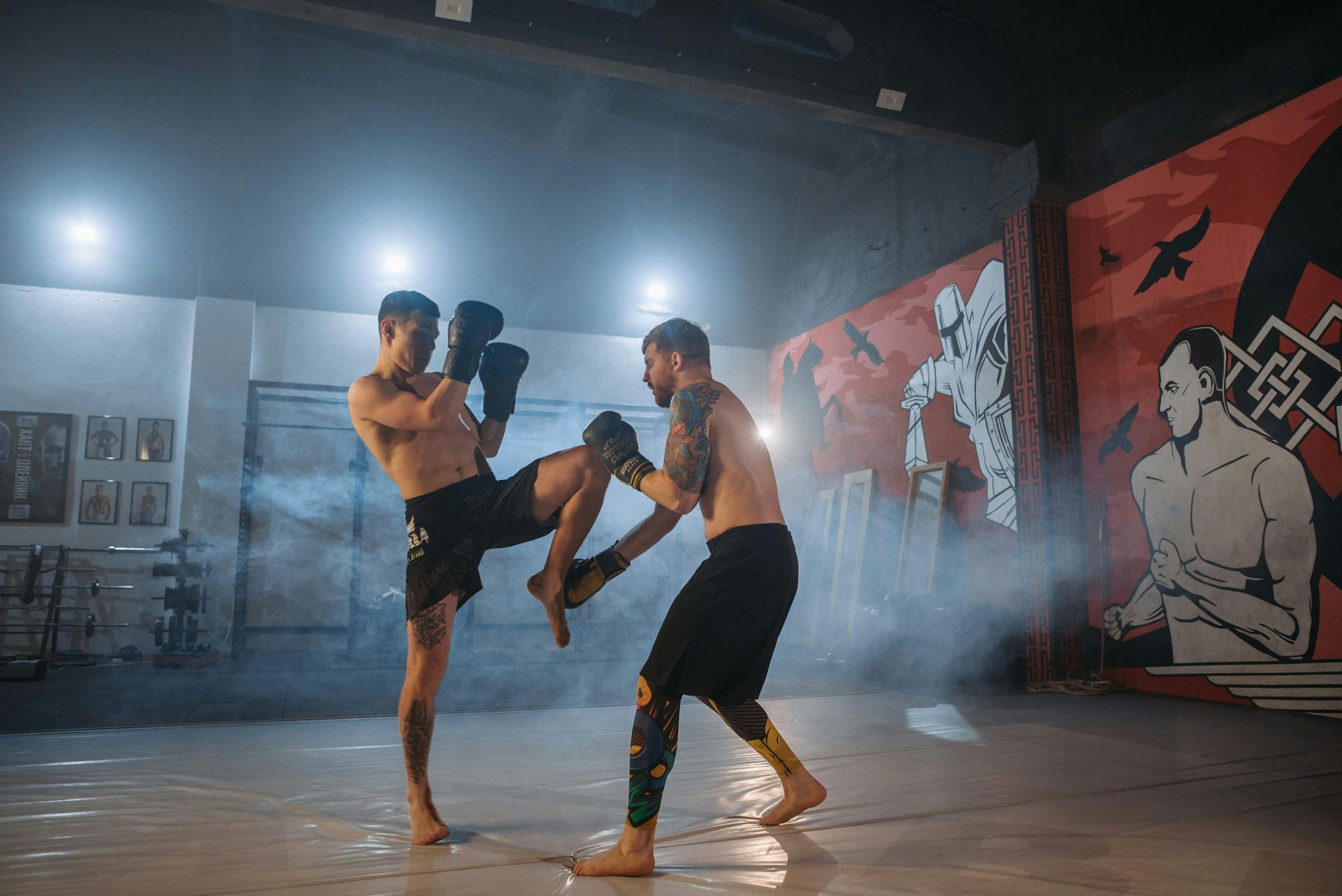 Two men sparring in a boxing ring; one kicking, the other blocking; smoky atmosphere with graffiti art.