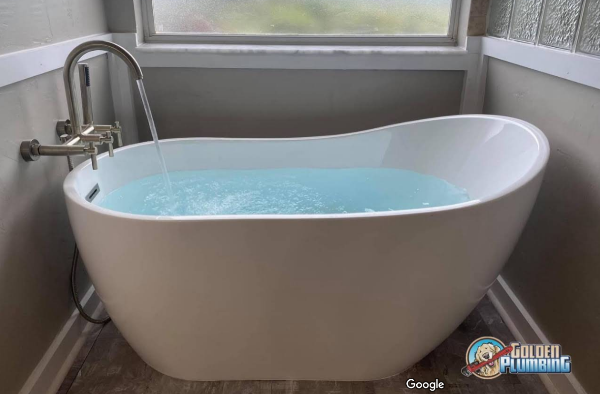 A bathtub filled with blue water is in a bathroom next to a window.