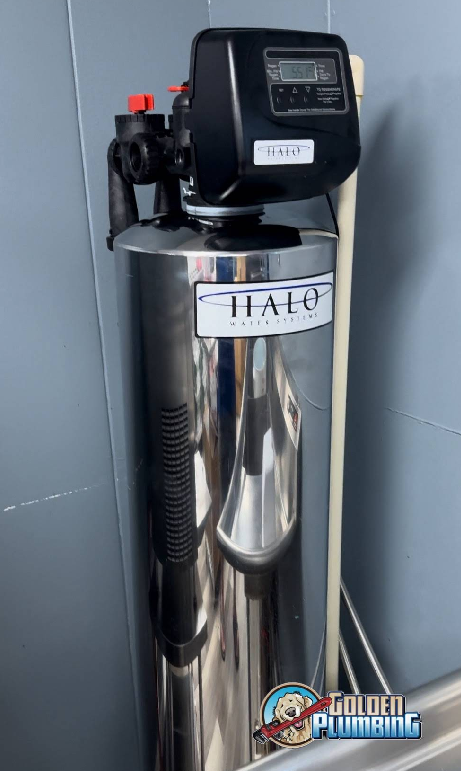 A stainless steel water filter is sitting on a counter next to a wall.