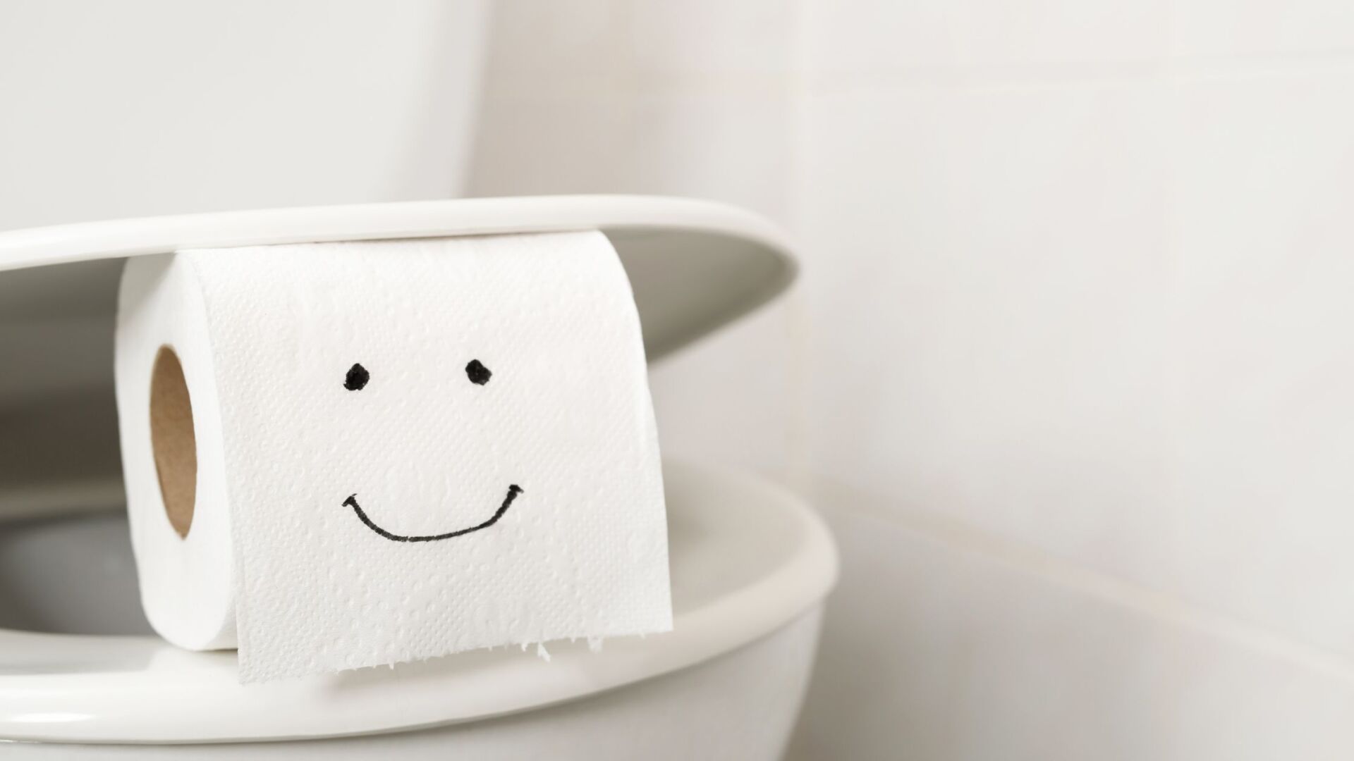 Toilet paper roll sitting on the edge of a toilet with a smile drawn on
