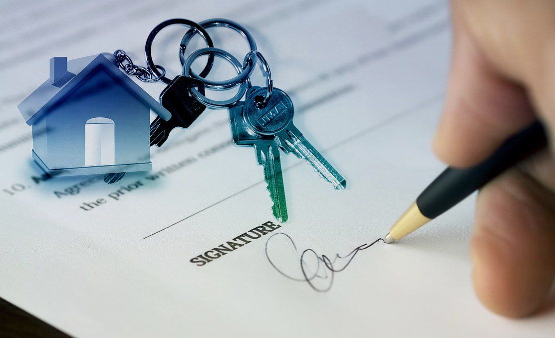 A hand signing a title transfer document at a real estate law firm.