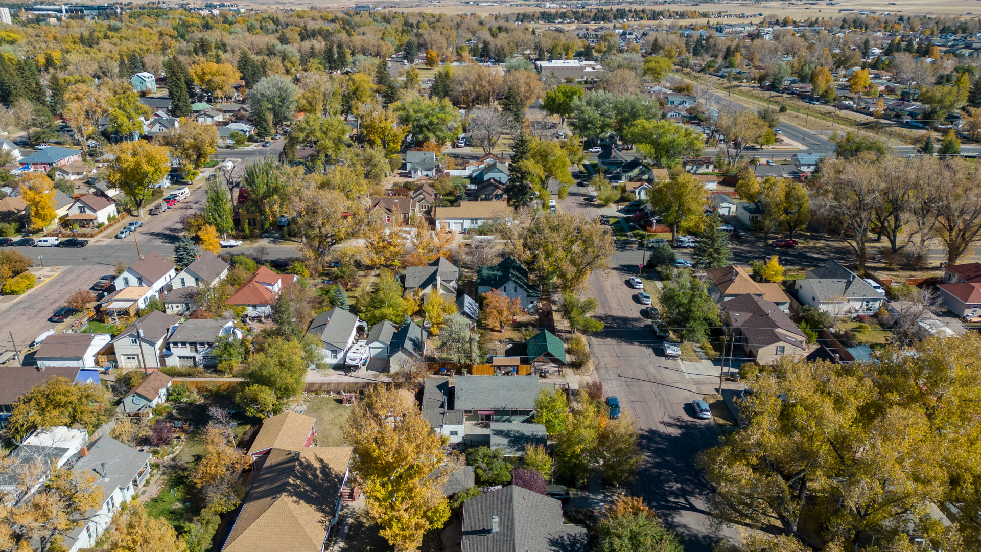 Aerial view of a residential neighborhood with houses, trees, and roads. Fall foliage in warm colors.