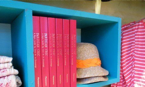 A hat sits on a shelf next to a row of pink books