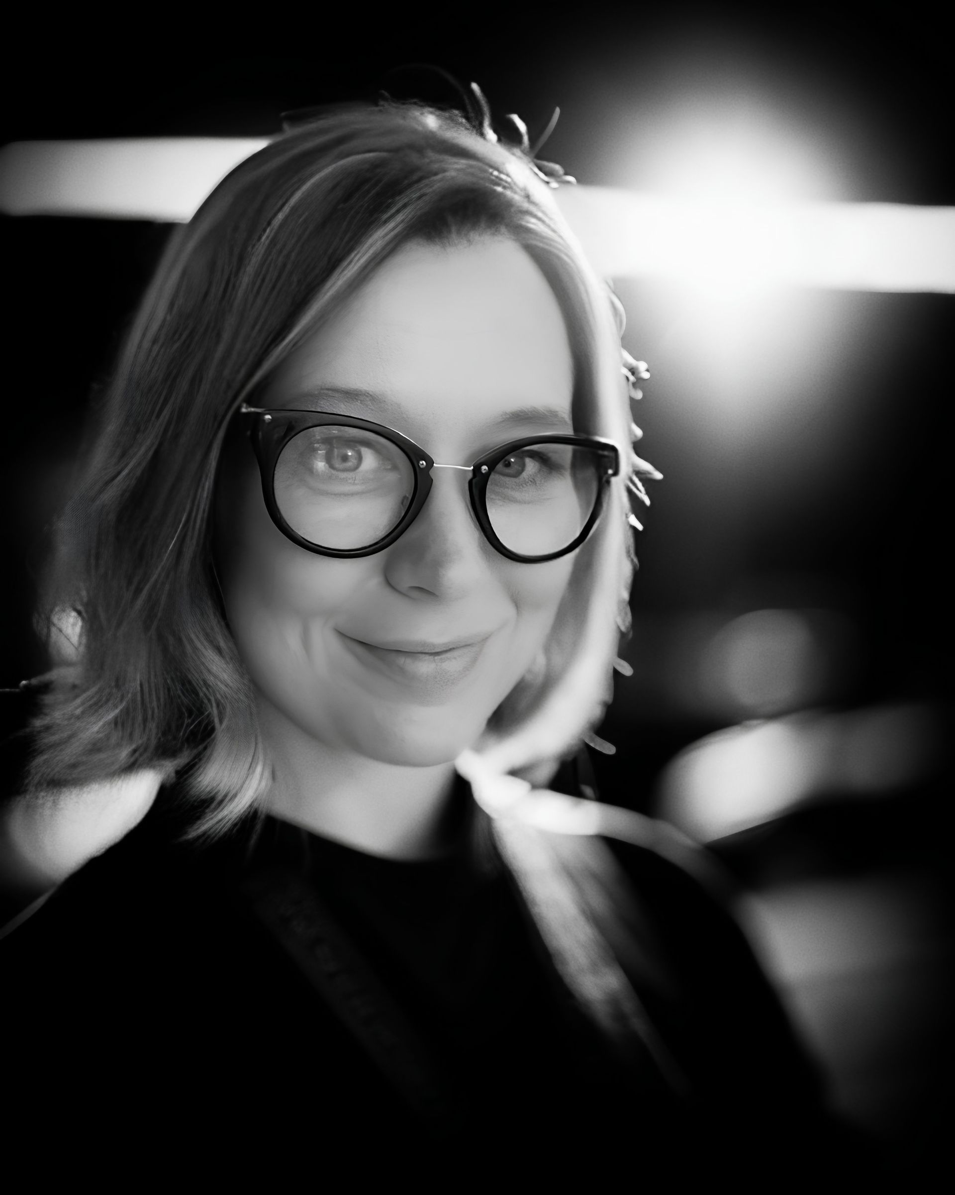 A woman wearing glasses and a white turtleneck is smiling for the camera.