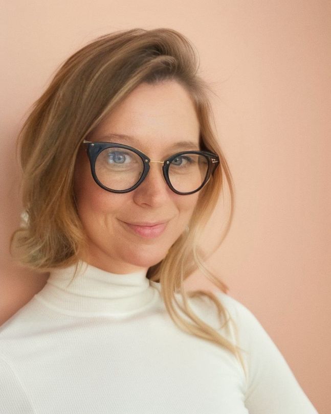 A woman wearing glasses and a white turtleneck is smiling for the camera.