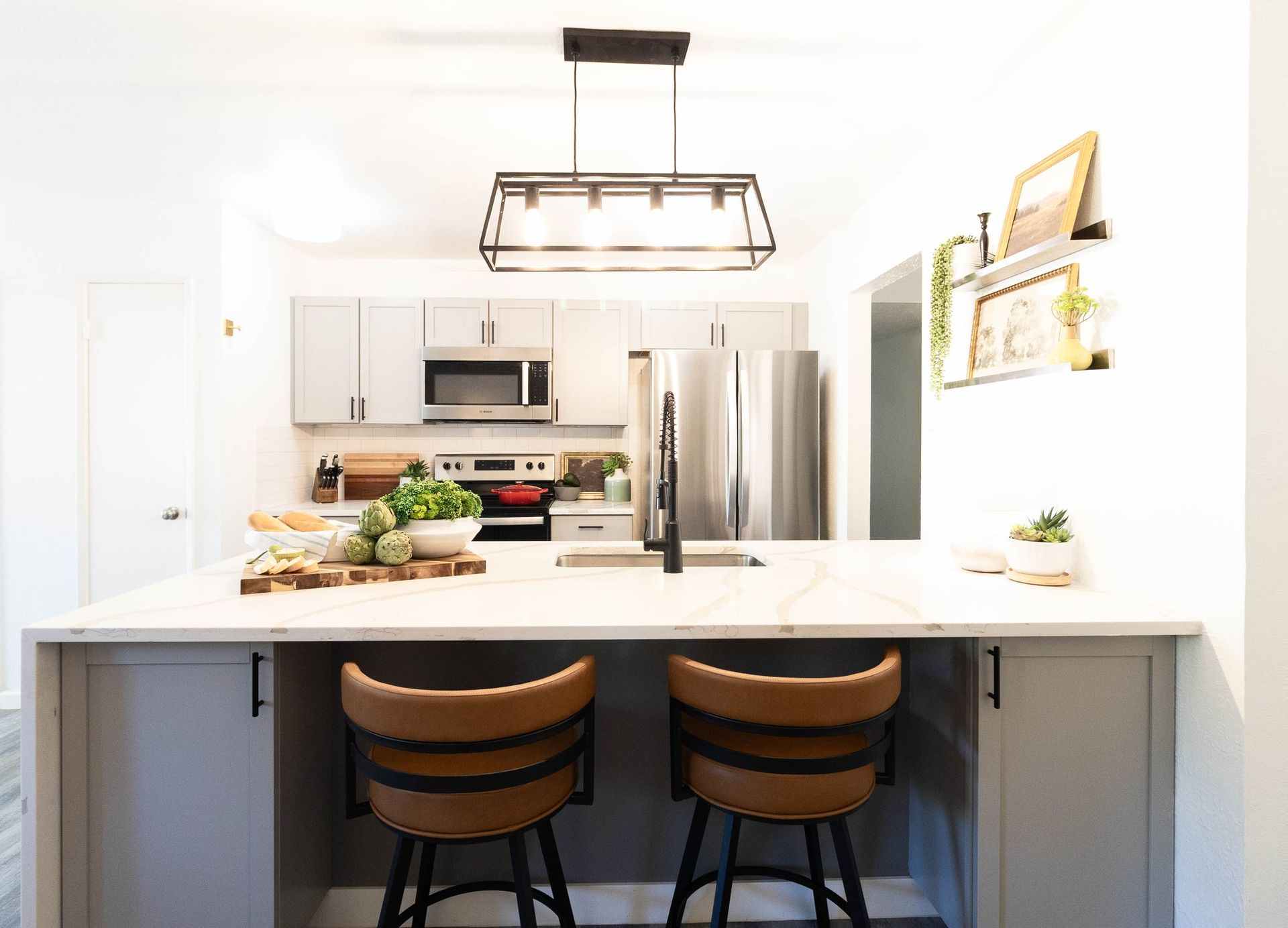 A kitchen with two bar stools and a stainless steel refrigerator.