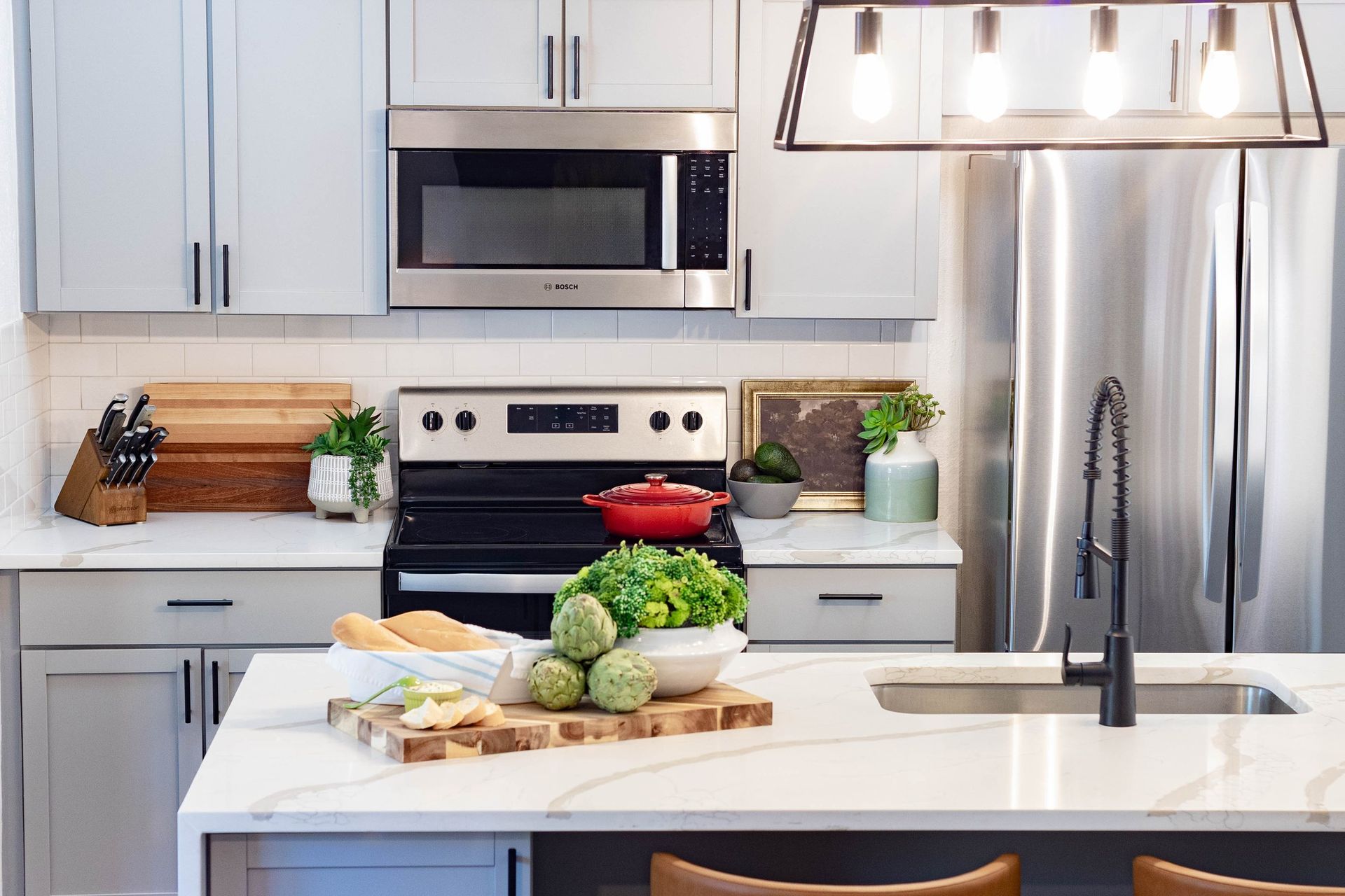 A kitchen with white cabinets , stainless steel appliances , a stove , microwave , refrigerator and sink.