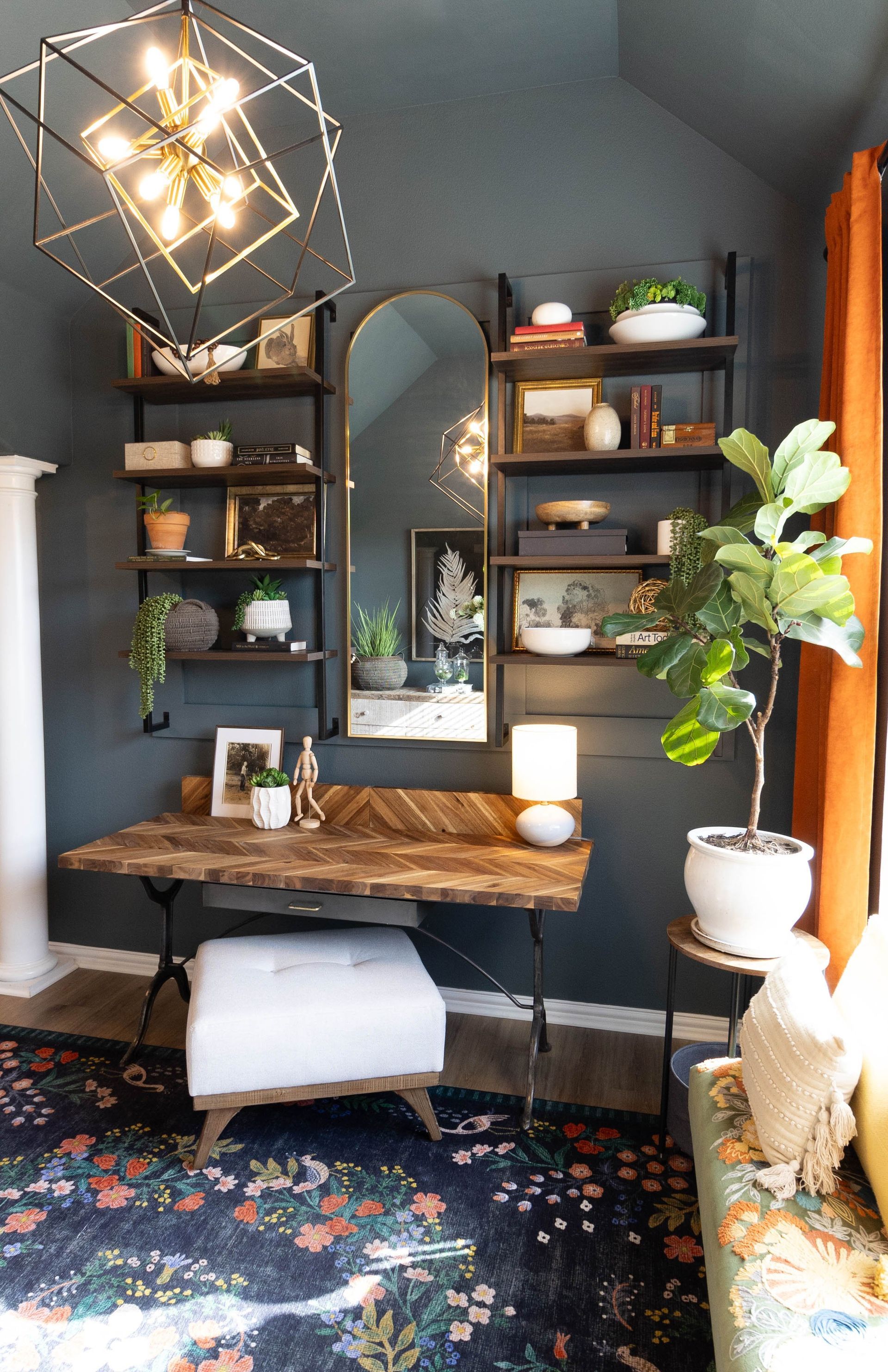 A room with a desk , ottoman , mirror and shelves.