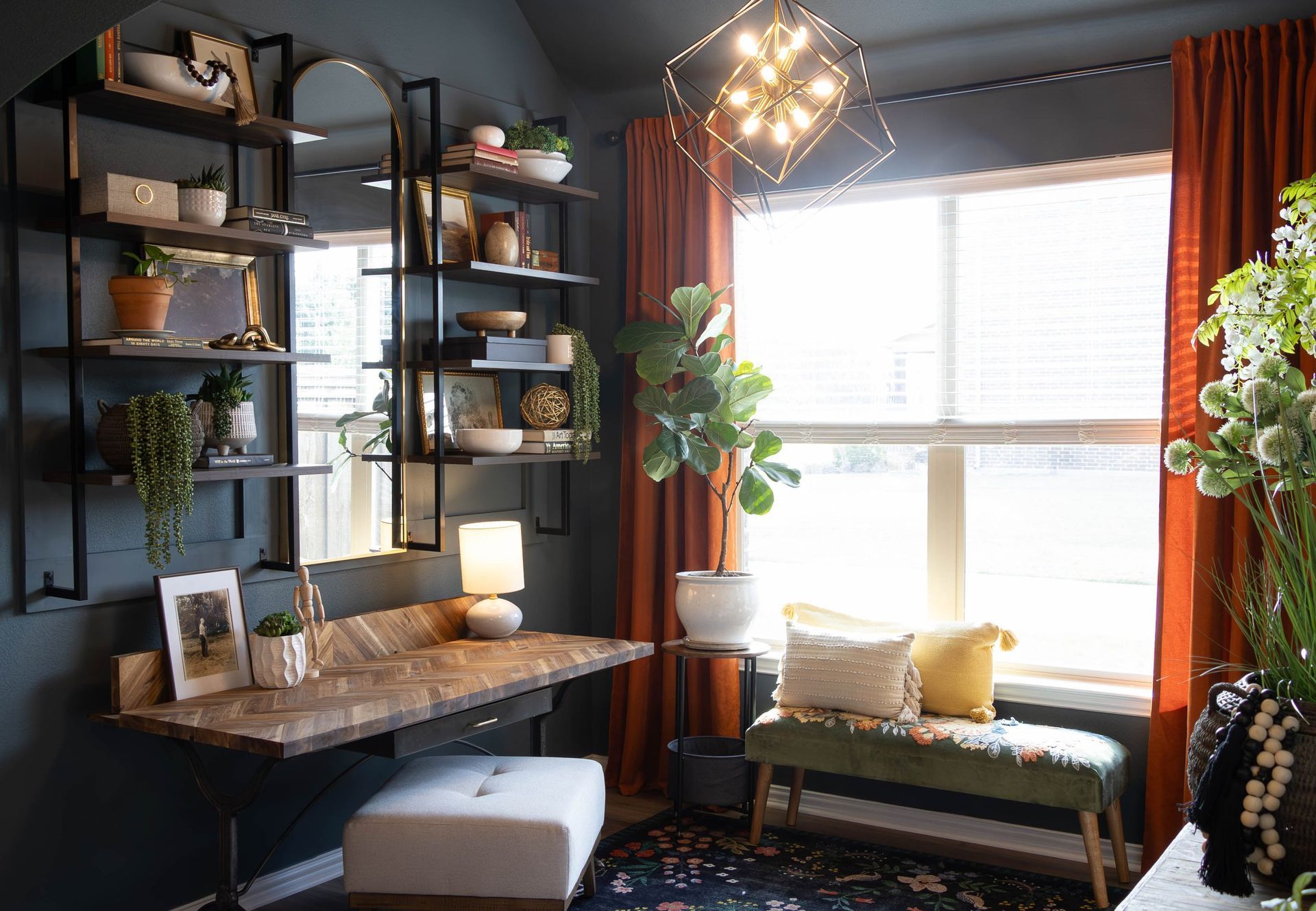 A living room with a desk , ottoman , window and shelves.