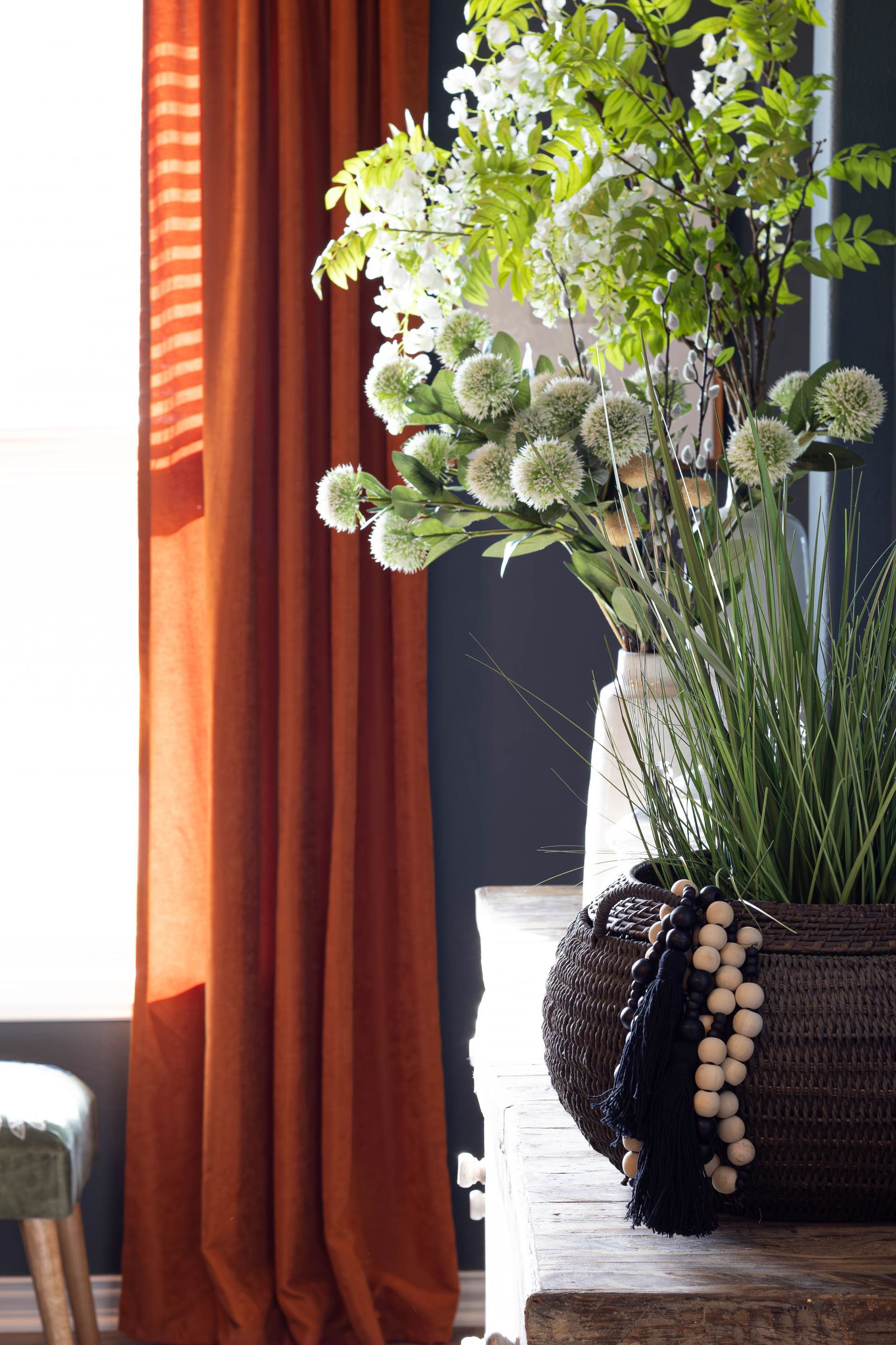 A vase of flowers sits on a table in front of orange curtains