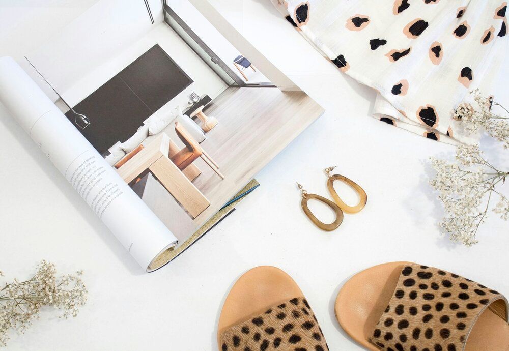 A pair of sandals , earrings , a magazine , and a dress are on a table.