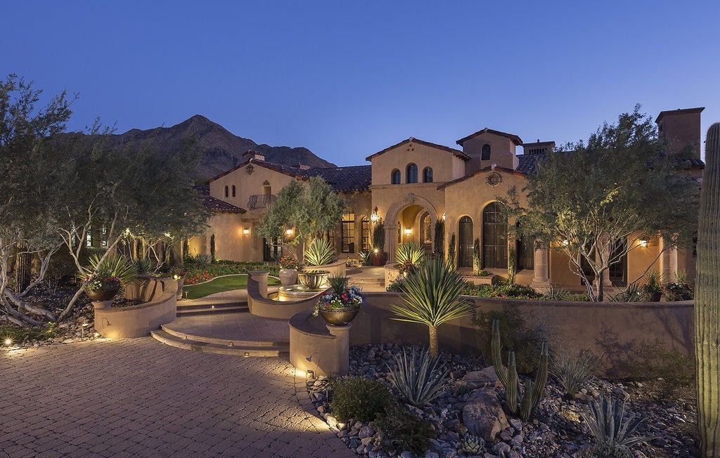 A large house with mountains in the background is lit up at night
