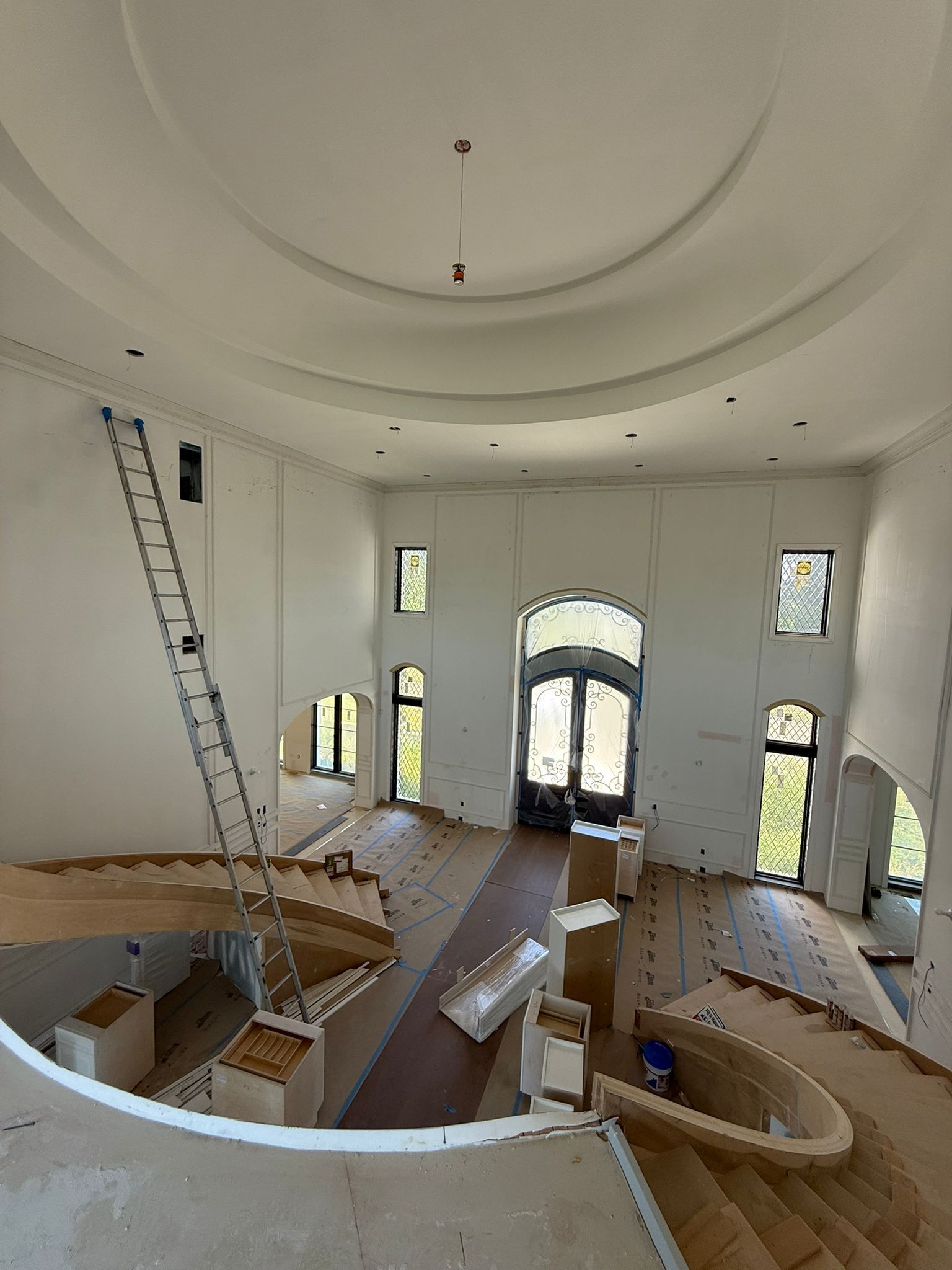 High-angle view of a large, unfinished foyer featuring dual curved staircases, tall windows, and a circular tray ceiling in New Jersey