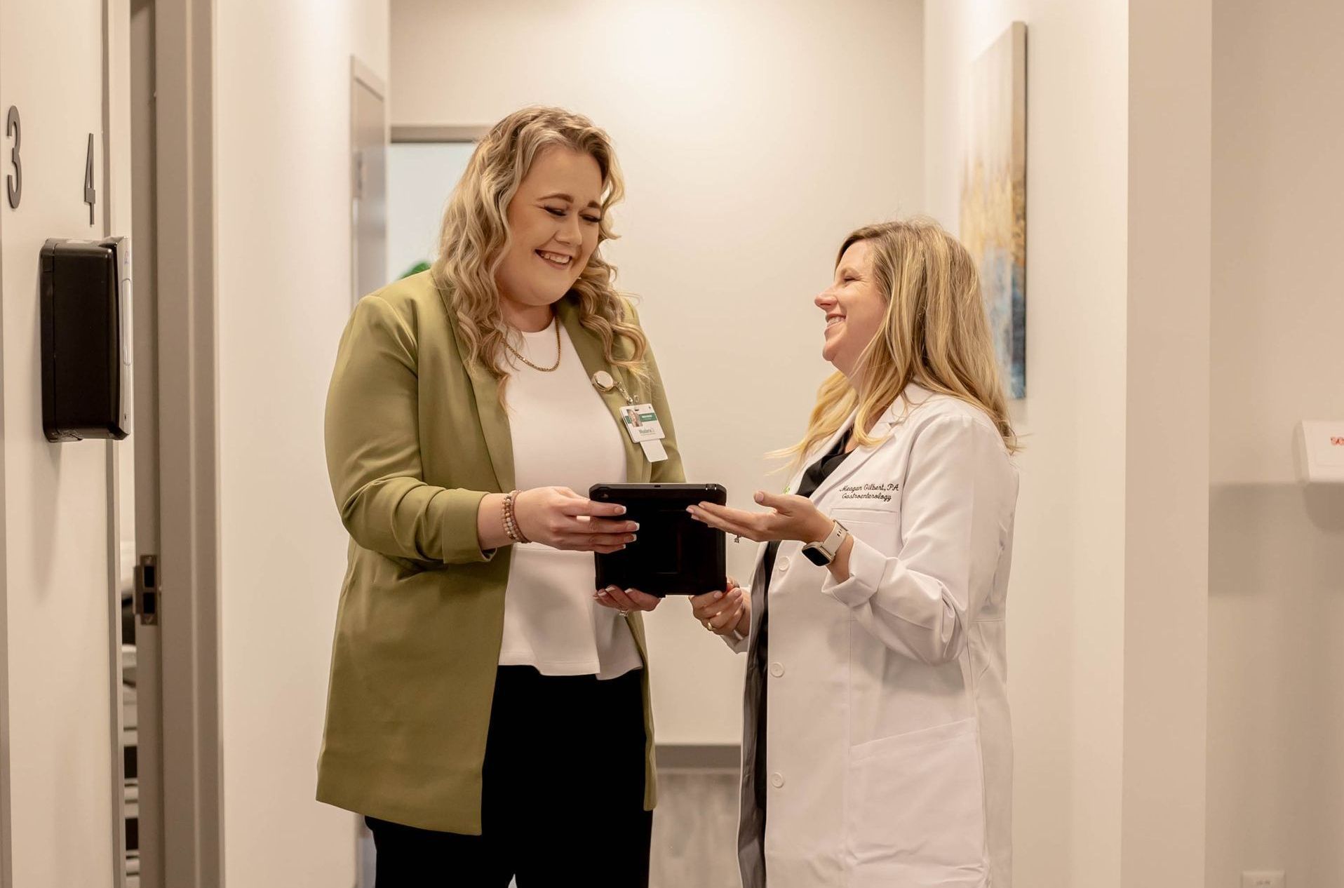 two women holding a conversation while holding a tablet in a corridor