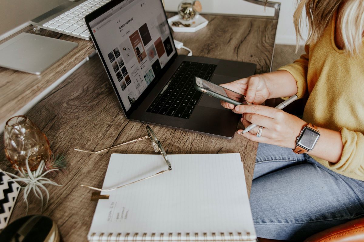 A woman is sitting at a desk with a laptop and a cell phone.