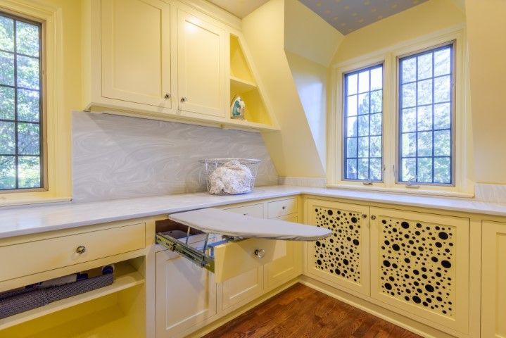 A laundry room with yellow cabinets and a folding ironing board.