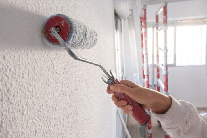 A person is painting a wall with a paint roller.