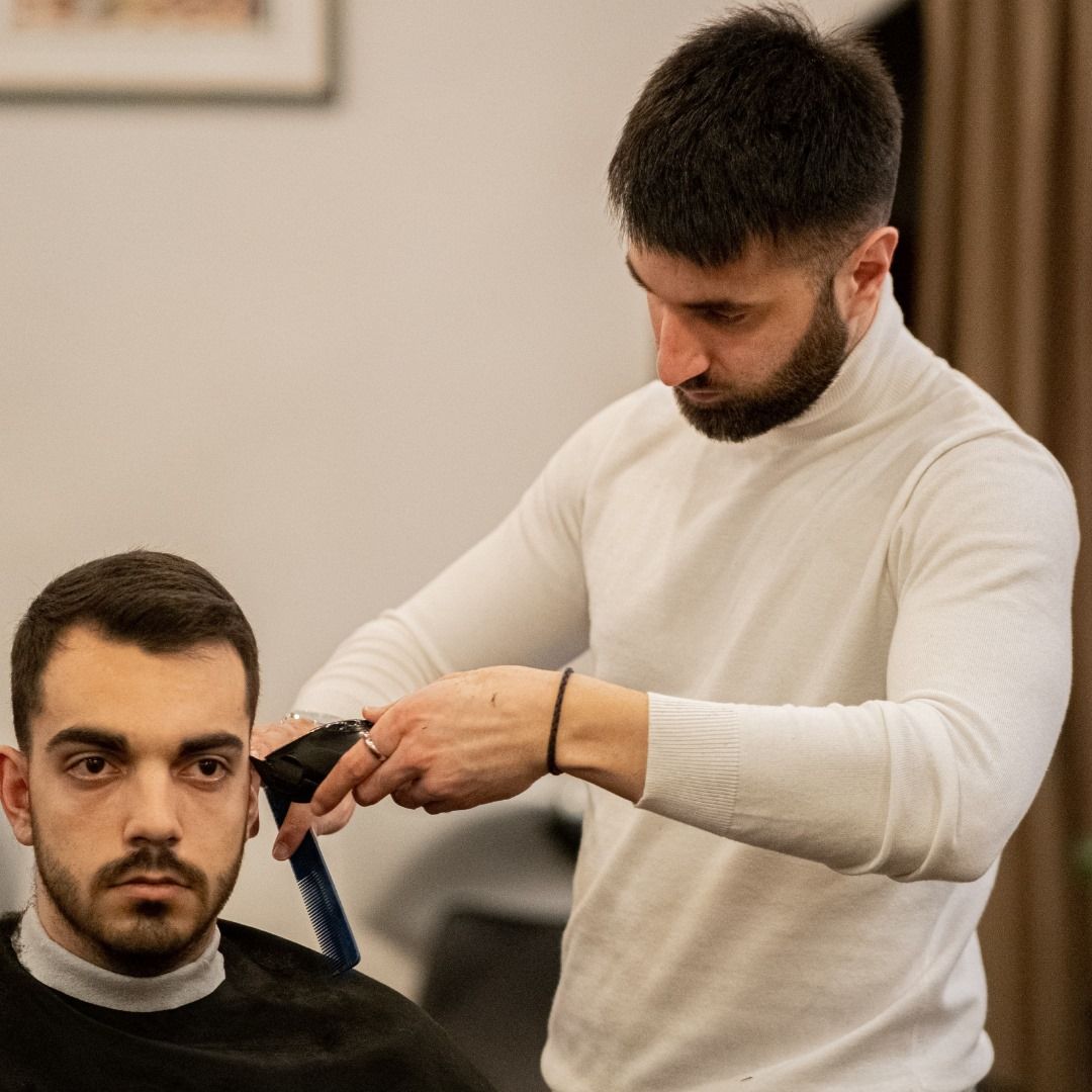 Un barbiere taglia i capelli a un uomo con il rasoio elettrico in un salone, entrambi concentrati sul taglio di capelli.