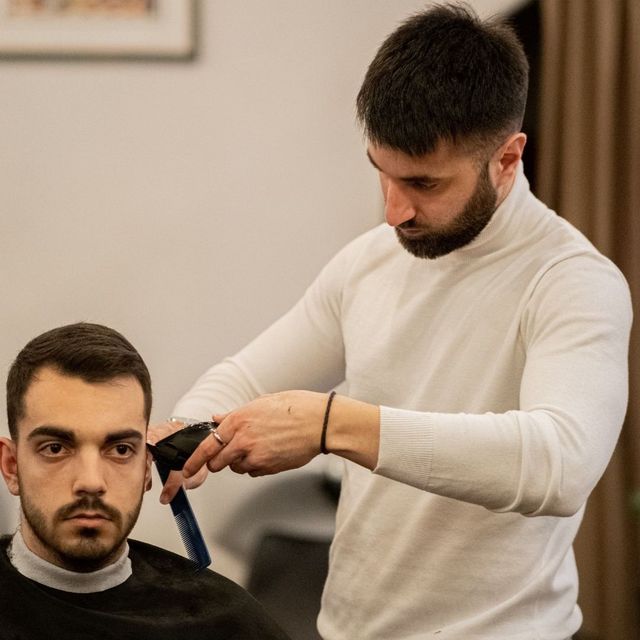 Un barbiere taglia i capelli a un uomo con il rasoio elettrico in un salone, entrambi concentrati sul taglio di capelli.