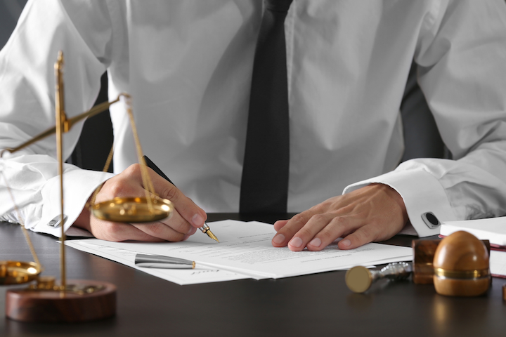 A lawyer signing a document with the scales of justice on his desk.