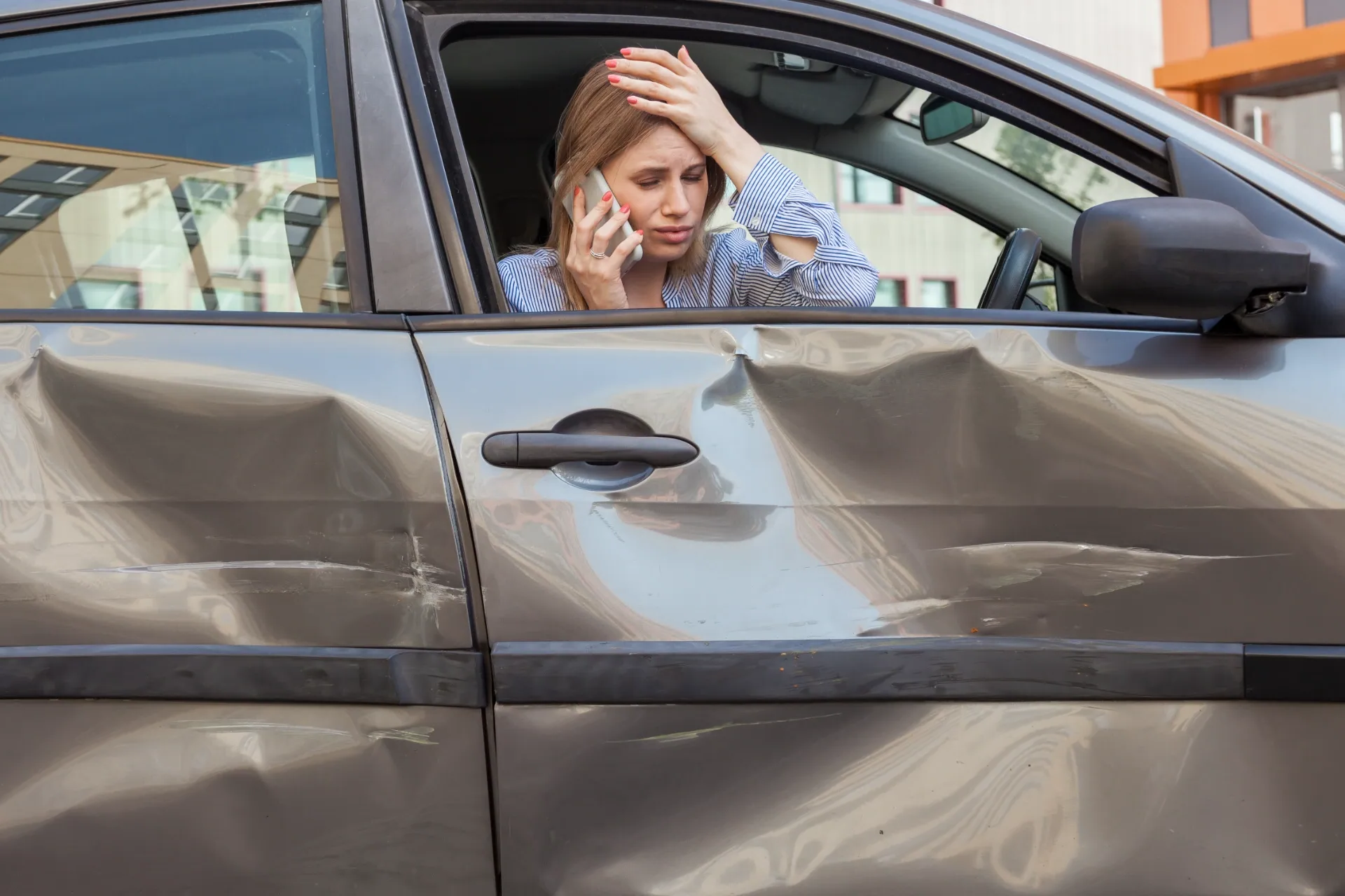 A person sits in a car with heavy door damage, looking distressed while talking on a mobile phone with a hand on their head. — Dwyer Law Group in Surfers Paradise, QLD